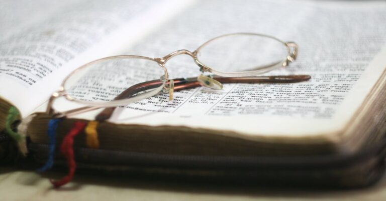 Close-up of eyeglasses atop an open Bible with colorful bookmarks, ideal for religious study themes.