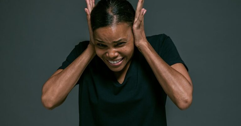 Portrait of an adult woman covering ears, looking irritated, against a dark background.