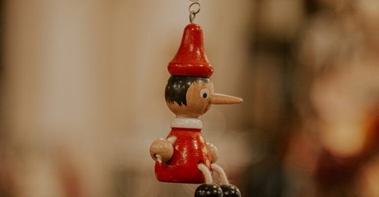 Detailed wooden Pinocchio ornament hanging amidst blurred festive decorations, embodying holiday charm.