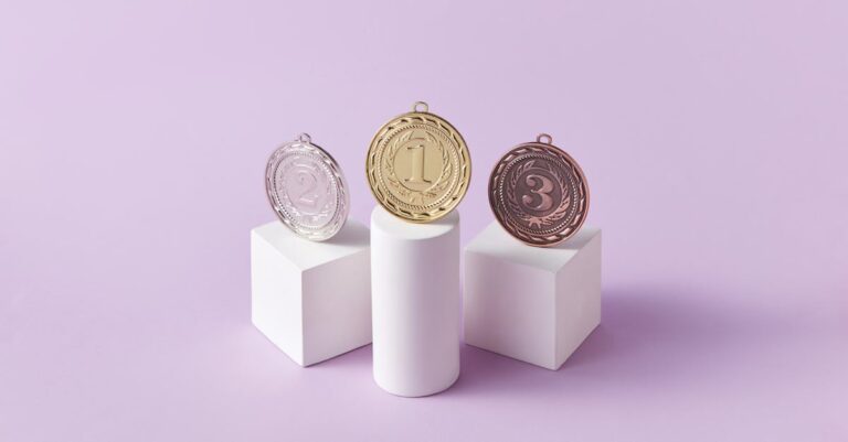 Gold, silver, and bronze medals displayed on white pedestals with a pink background.