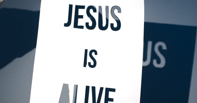 A person holding a white paper with the message 'Jesus is Alive' against a blue background.