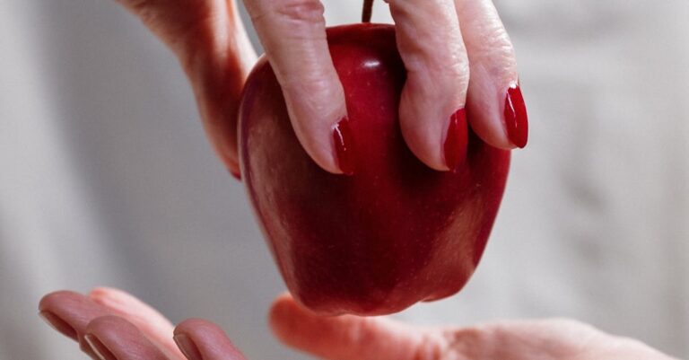 A close-up of two hands exchanging a red apple, symbolizing temptation or stories like Snow White.