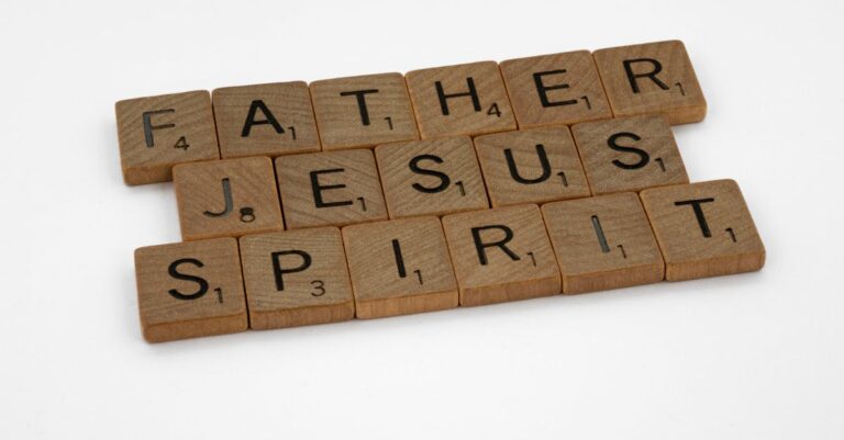 Wooden Scrabble tiles displaying 'Father,' 'Jesus,' and 'Spirit' on a white background.